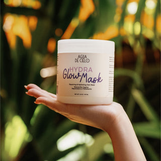 A hand holding a white tub of best hair mask for bleached hair and colored hair