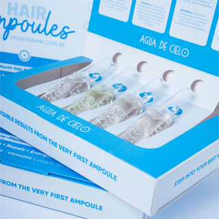Open white and blue box of hair ampoule treatment for damaged hair with several clear glass ampoules inside. The packaging shows the text 'HAIR AMPOULES', 'AGUA DE CIELO', and 'VISIBLE RESULTS FROM THE VERY FIRST AMPOULE'.