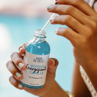 Hair growth kit - A close-up of a person holding a glass bottle of hair energizing drops with a dropper, with a blurred outdoor background.