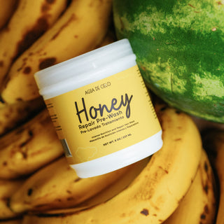 A jar of AGUA DE Cielo Honey Repair Pre-Poo pre-loved treatment lotion, styled with fresh bananas and a watermelon in the background.