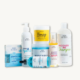 A nourishing hair treatment from Agua de Cielo arranged on a light off-white background. The products include a Hydrate Hair pump bottle, a Honey hair mask jar, a Recover Me Shampoo bottle, an Everything Serum spray, a blue Energizer mask bottle, an Ampollas box, and a blue serum dropper bottle.