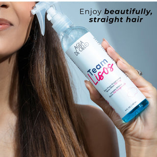 A woman holds a bottle of Aqua de Cielo Team Lisos straightening spray for hair while straightening her long brown hair. The bottle is white with blue and pink lettering, and the text 'Enjoy beautifully, straight hair' appears at the top right.